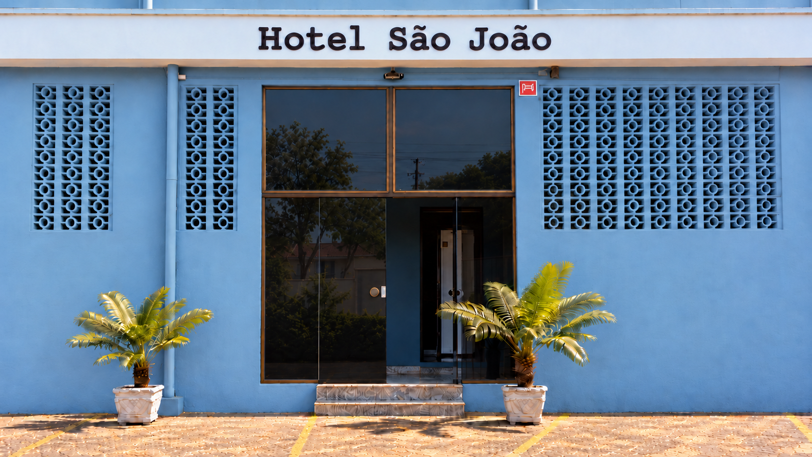 Entrada do Hotel São João, fachada azul com porta de vidro e palmeiras